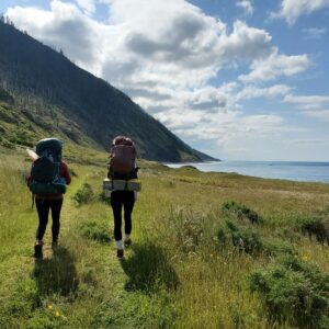Hikers walking on the trail with green grass surrounding the field and the ocean to their right side
